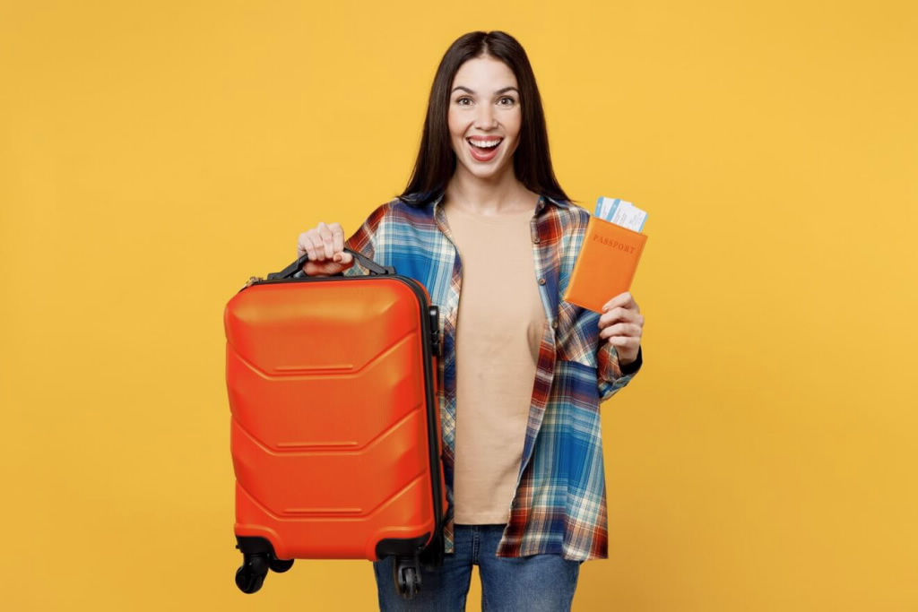 mujer sonriendo sosteniendo una maleta con una mano y con la otra, un billete de avion